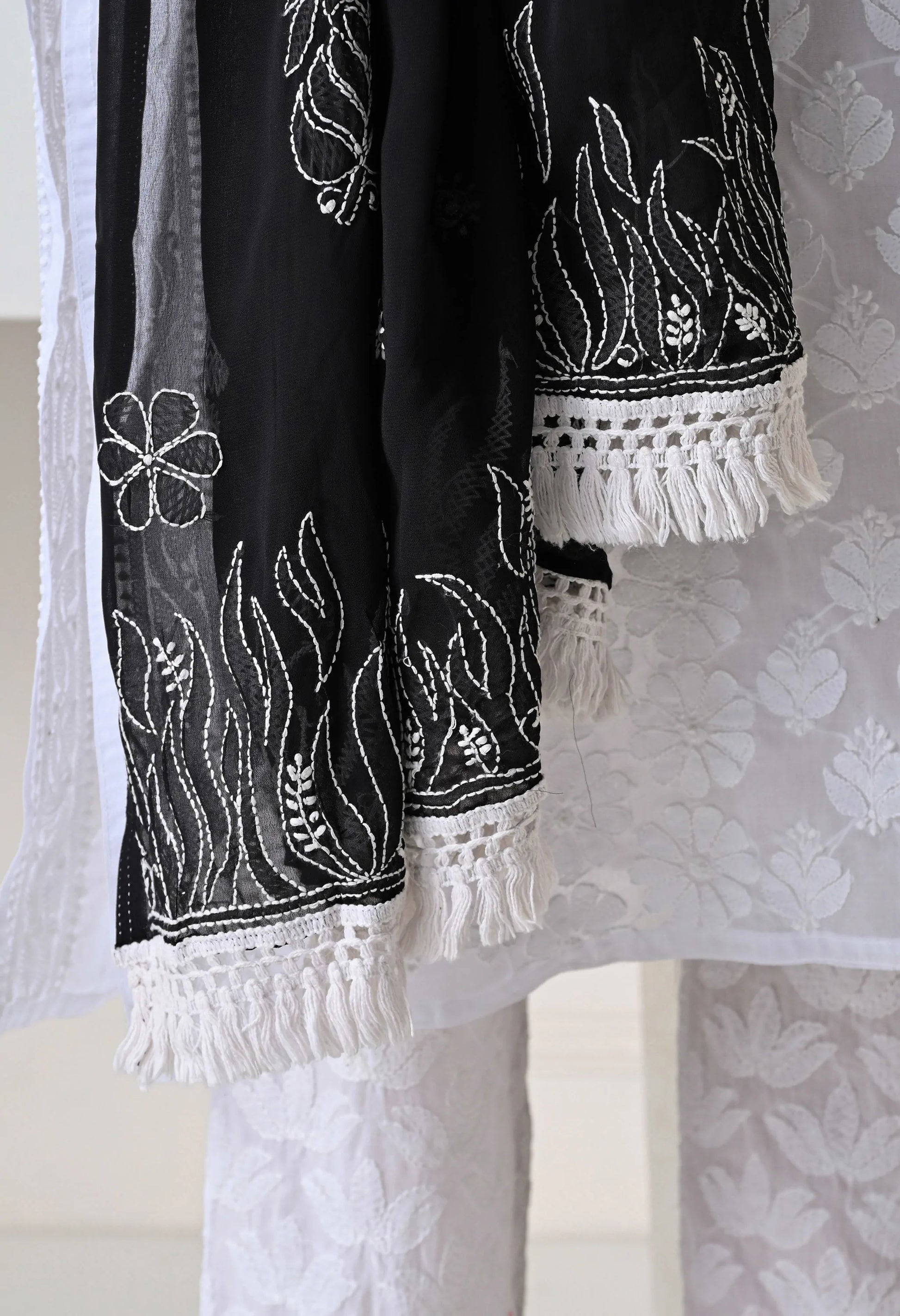 Black and white embroidered fabric dupatta with tassels on a textured background
