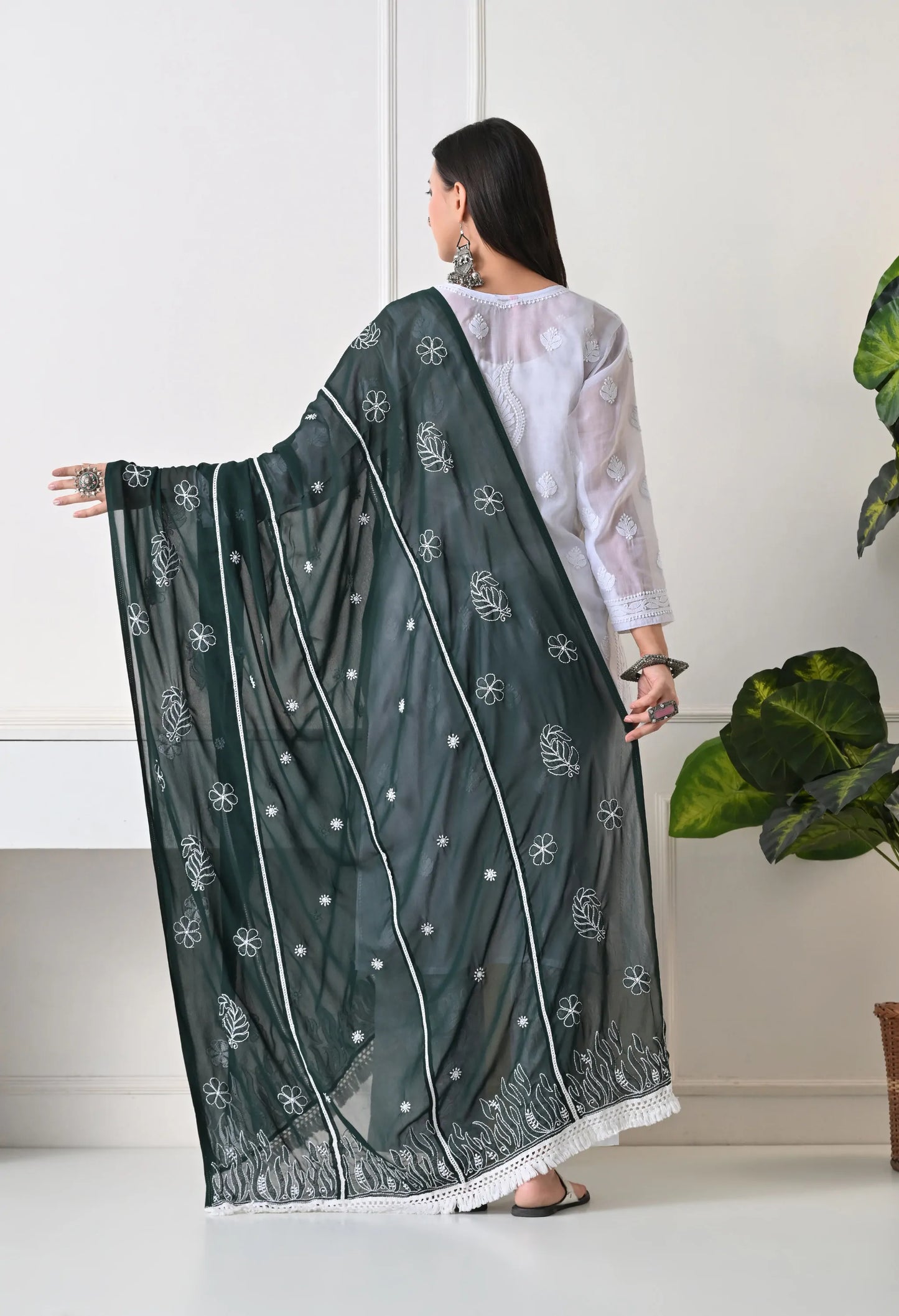 Woman holding a bottle green embroidered scarf in a minimal indoor setting