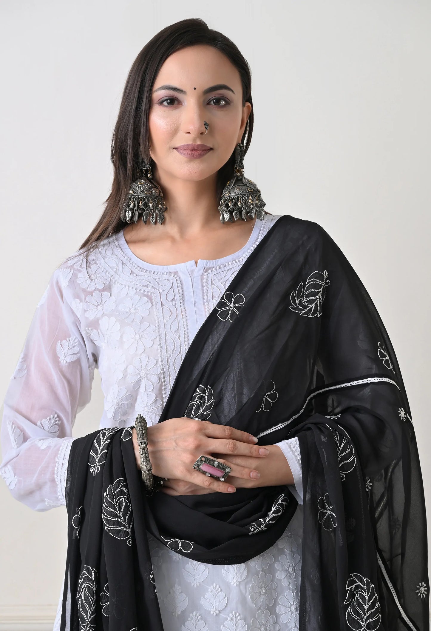 Woman wearing a black embroidered dupatta over a white outfit against a plain background
