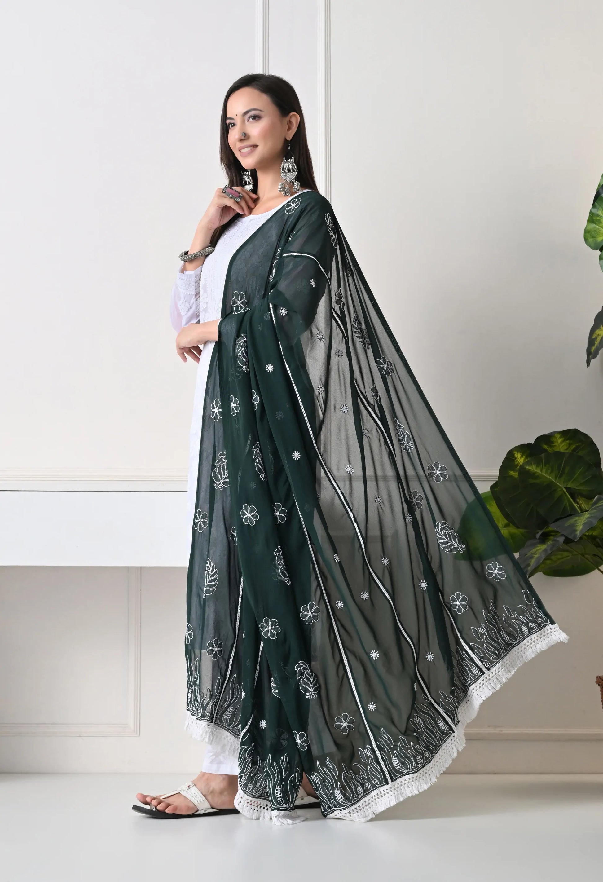 Woman wearing a bottle green saree with white patterns on a white background