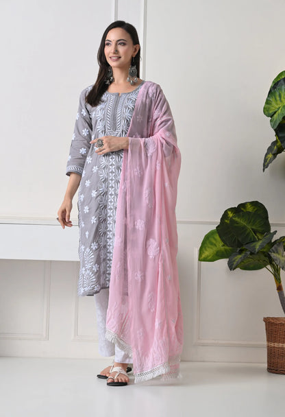 Woman wearing a light gray and white embroidered outfit with a pink dupatta, standing indoors.