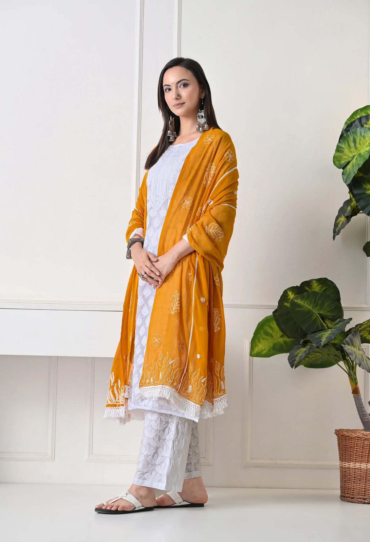 Woman wearing a mustard yellow dupatta over a white outfit in a minimal indoor setting.