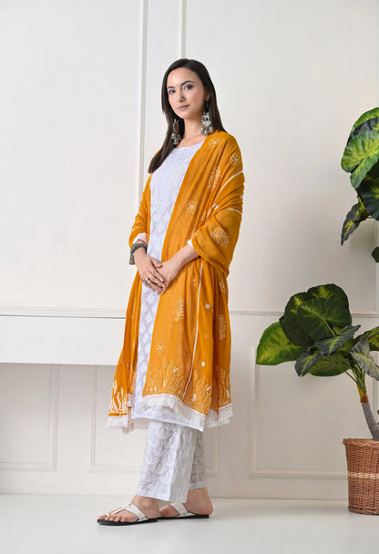 Woman wearing a mustard yellow dupatta over a white outfit in a minimal indoor setting.