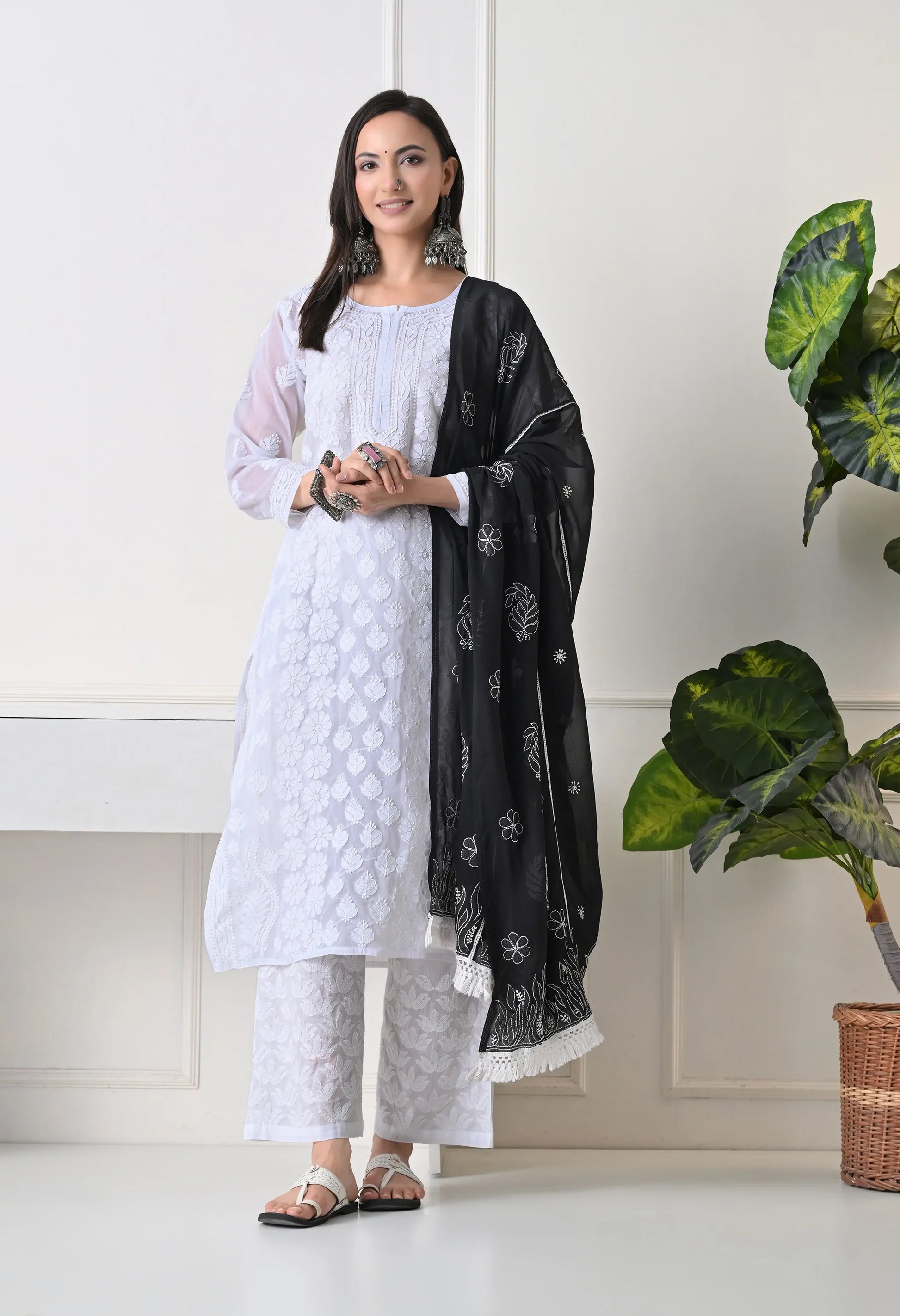 Woman wearing a white outfit with a black dupatta standing indoors.