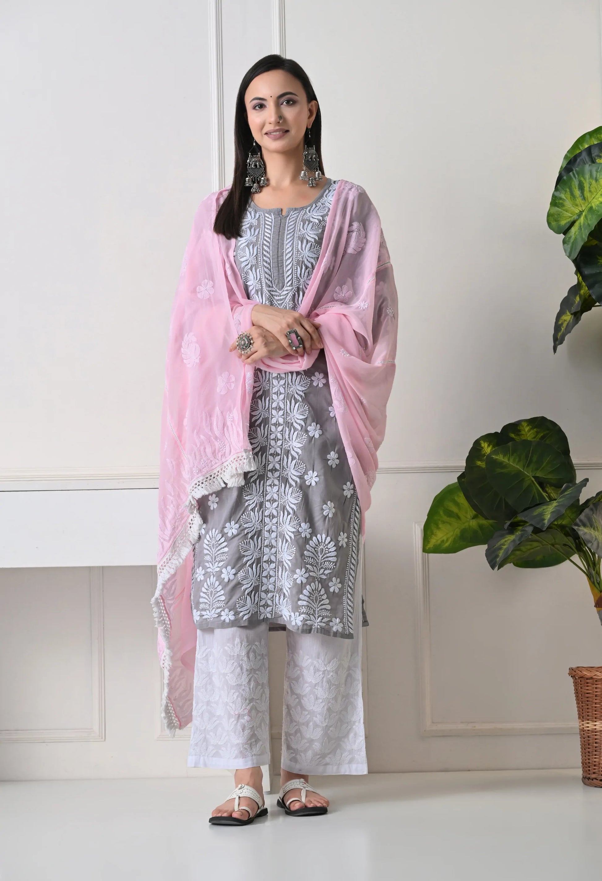 Woman wearing a gray floral dress with a pink dupatta in a minimal indoor setting.