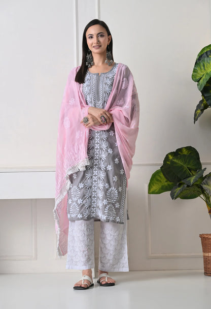 Woman wearing a gray floral dress with a pink dupatta in a minimal indoor setting.