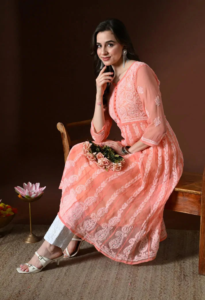 Seated model wearing peach embroidered anarkali kurta set with white pants