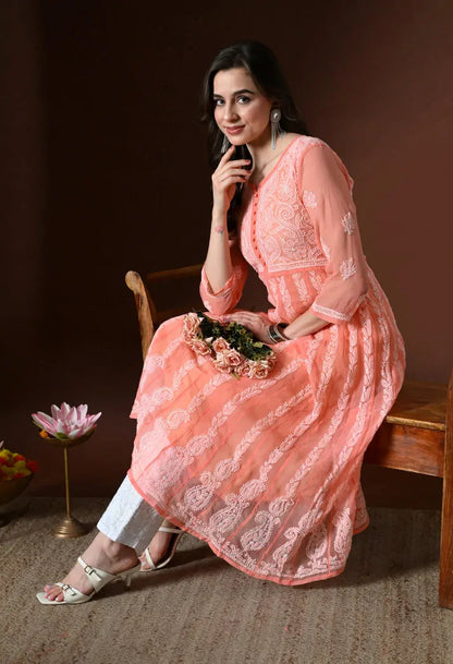 Seated model wearing peach embroidered anarkali kurta set with white pants